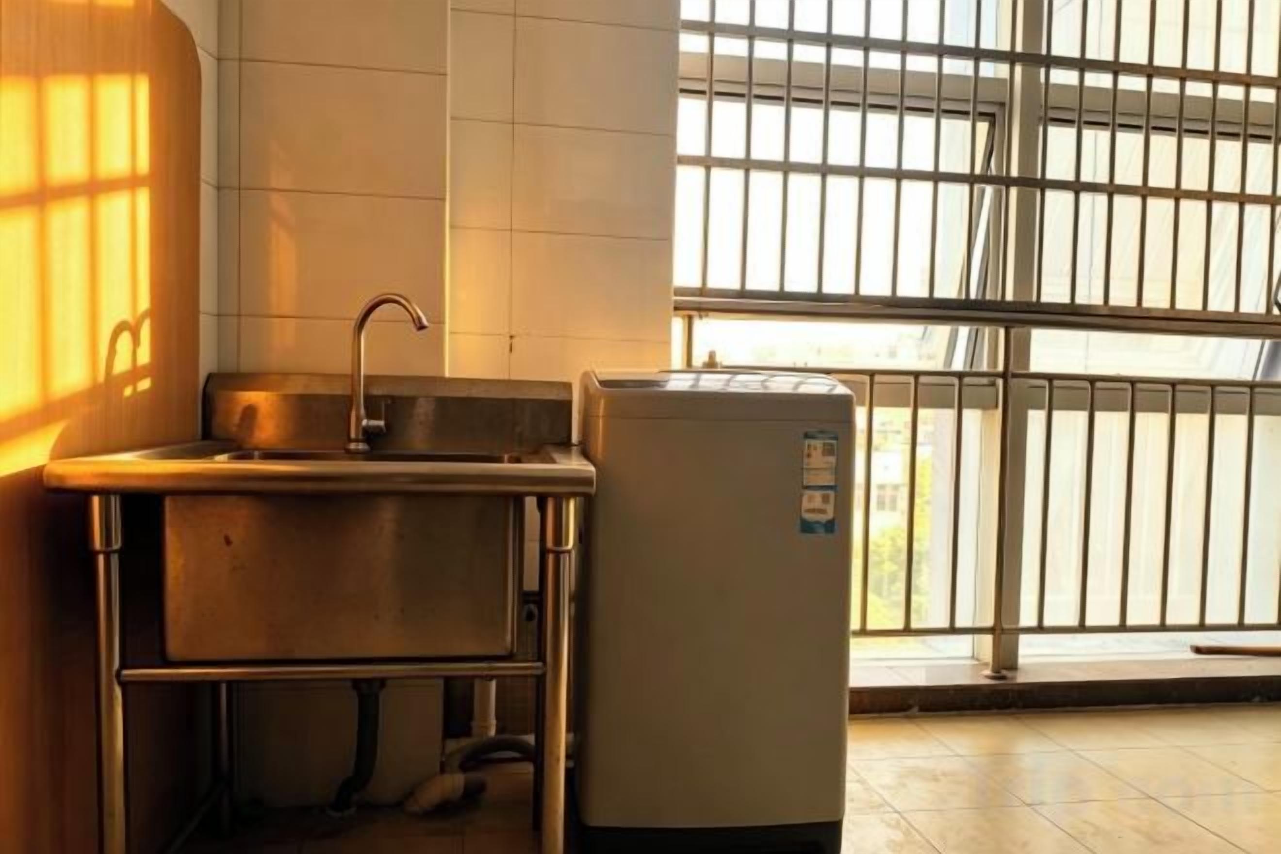 A kitchen with a sink, a refrigerator, and a window with bars.
