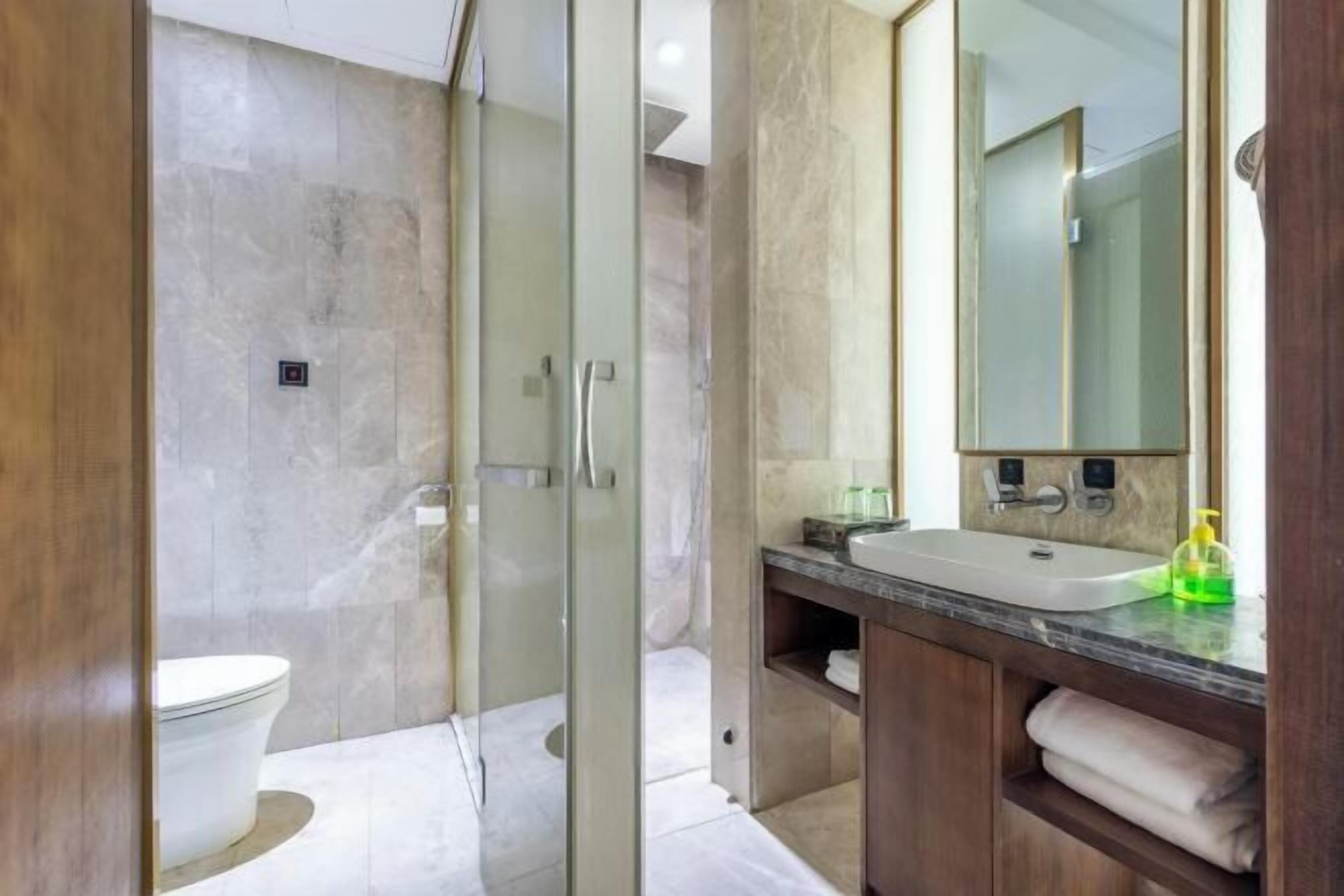 Ein modernes Badezimmer mit einer gläsernen Duschkabine, einer weißen Toilette, einem großen Waschbecken und einem hölzernen Waschtisch.