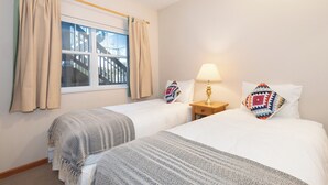 A hotel room with two beds, a window with curtains, a nightstand with a lamp, and a view of a building outside. - Deer Run by Whistler Premier (Whistler)