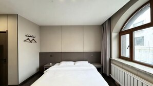 A modern hotel room with a large bed, a nightstand, a window with a view, and a coat rack. - Hongfu Business Rooms (Panshi)
