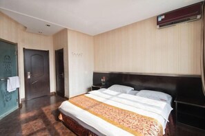 A hotel room with a large bed, a dark headboard, a wooden floor, and a door with a towel hanging on it. - Hongfu Business Rooms (Panshi)