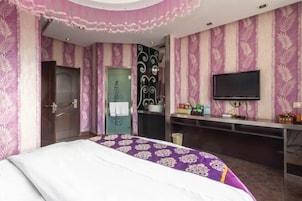 Una habitación de hotel con una cama, televisión, escritorio y la puerta del baño.