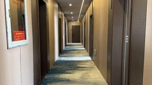 A hotel corridor with a carpeted floor, doors on both sides, and a fire safety sign on the left wall. - Hongfu Business Rooms (Panshi)