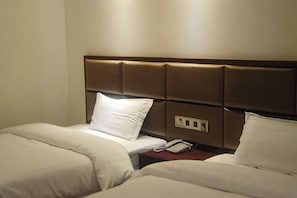 A hotel room with two beds, a headboard, a bedside table with a phone, and a power outlet.