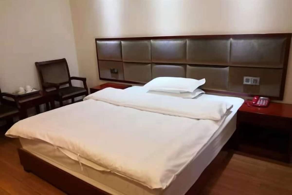 A hotel room with a large bed, a wooden nightstand, a chair, and a padded headboard.