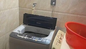 A washing machine with a control panel, a red basin, and a wall-mounted electrical outlet. - JUNLAISHUN HOTE (Ruijin)