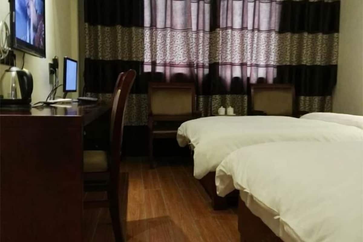 A hotel room with two beds, a desk with a computer, and a TV on the wall.