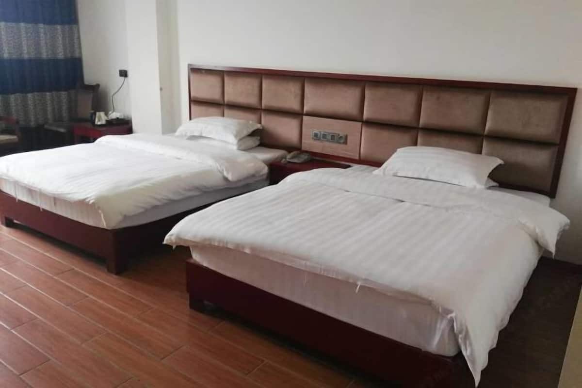 A hotel room with two beds, a wooden headboard, a bedside table with a phone, and a curtain.