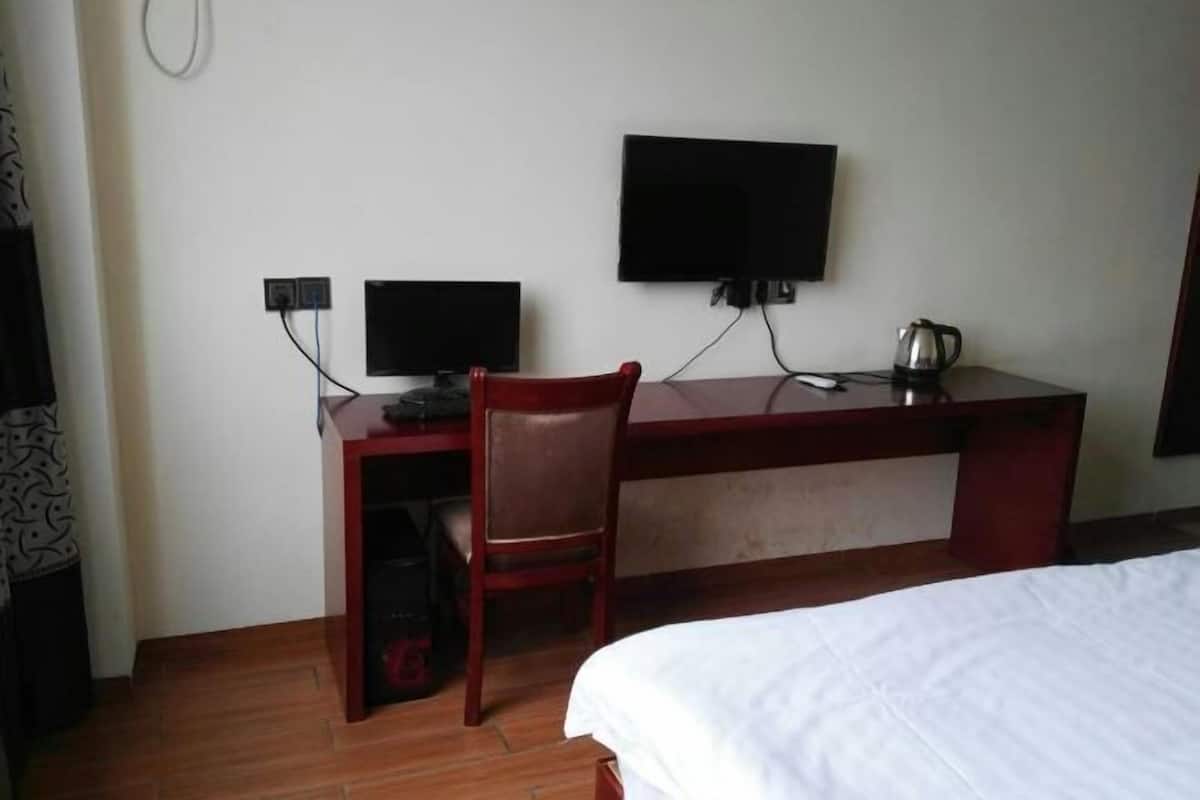 A hotel room with a bed, a desk with a chair, a television, and a kettle.
