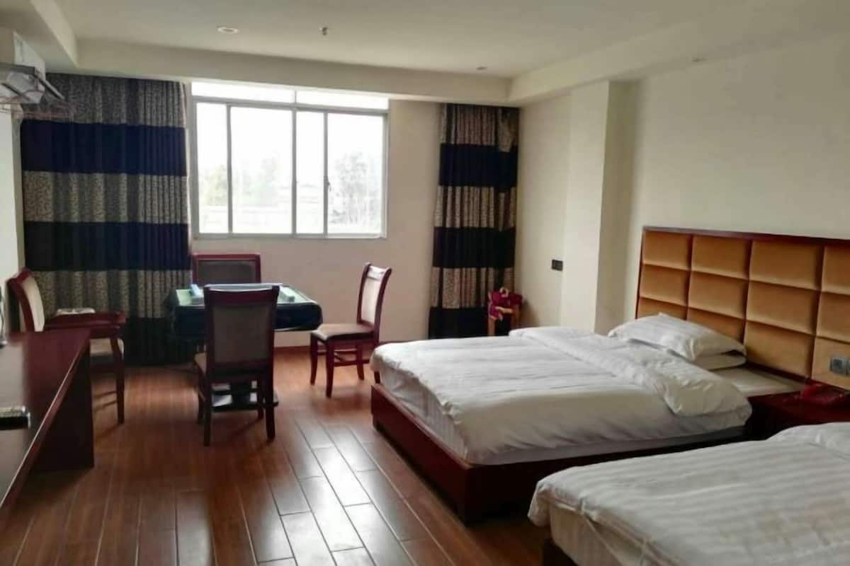 A hotel room with two beds, a desk, chairs, and a window.