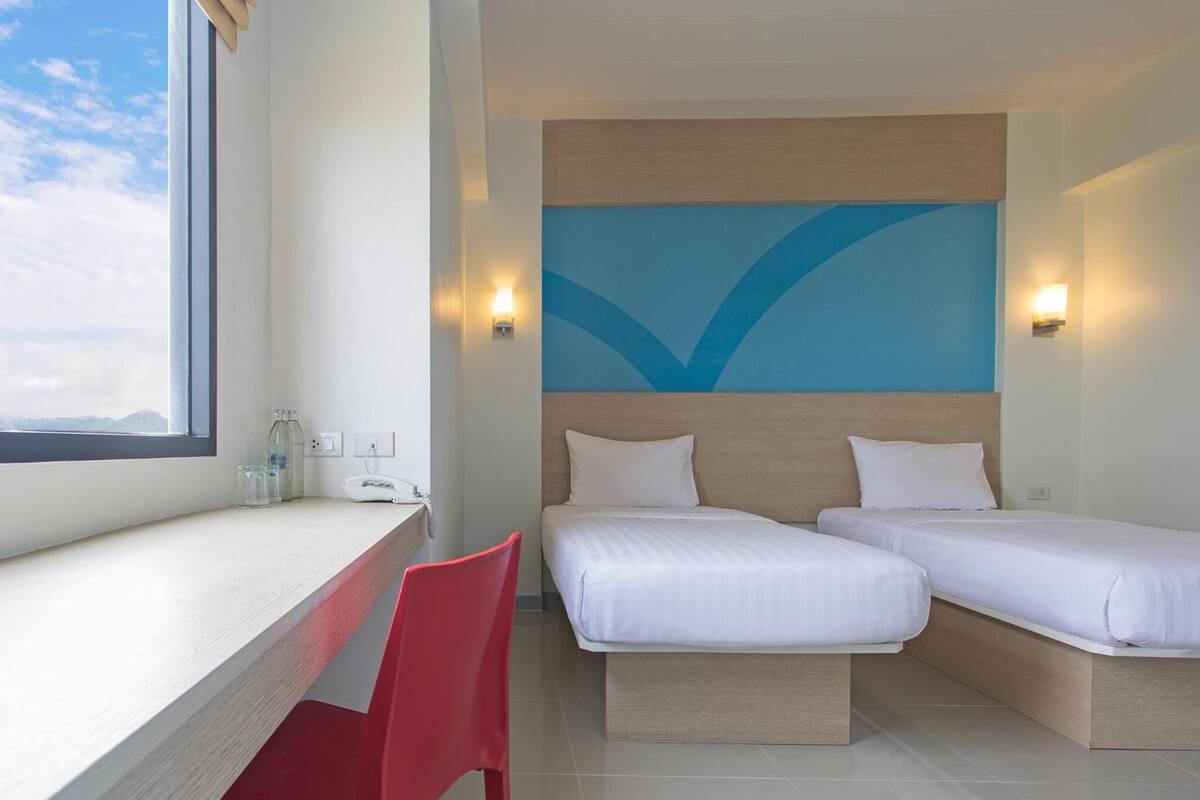 A hotel room with two beds, a desk, a red chair, and a view of the mountains.