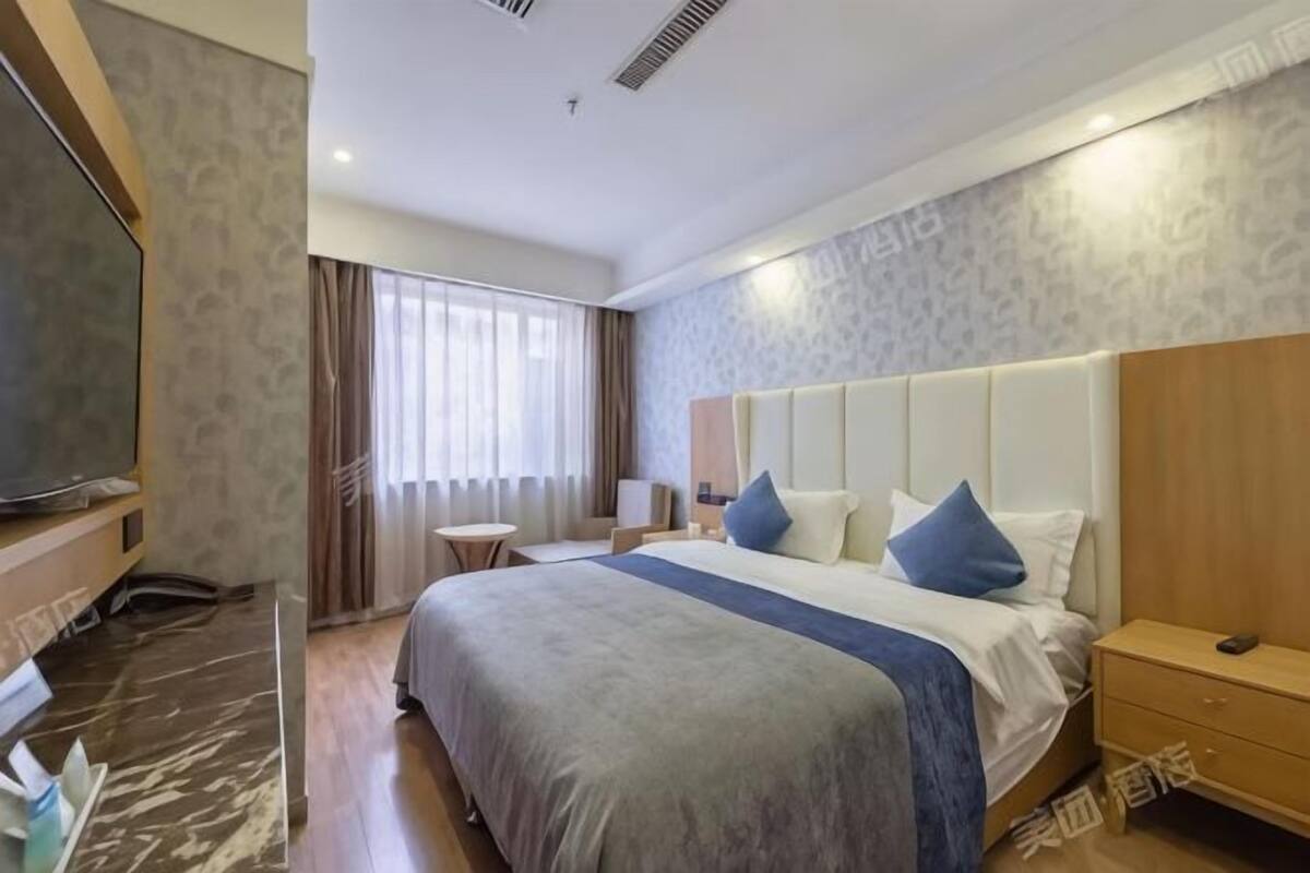 Habitación de hotel con cama, mesita de noche, televisor y ventana con cortinas.