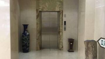 Um elevador com parede de mármore, um vaso e uma pequena mesa.