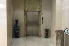 Een lift met een marmeren wand, een vaas en een kleine tafel.