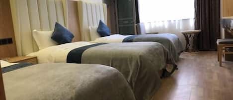 Habitación de hotel con tres camas, una mesita y vistas al exterior.