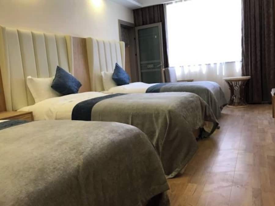 A hotel room with three beds, a small table, and a view of the outdoors.