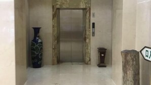 Un ascensor con pared de mármol, un jarrón y una mesita.