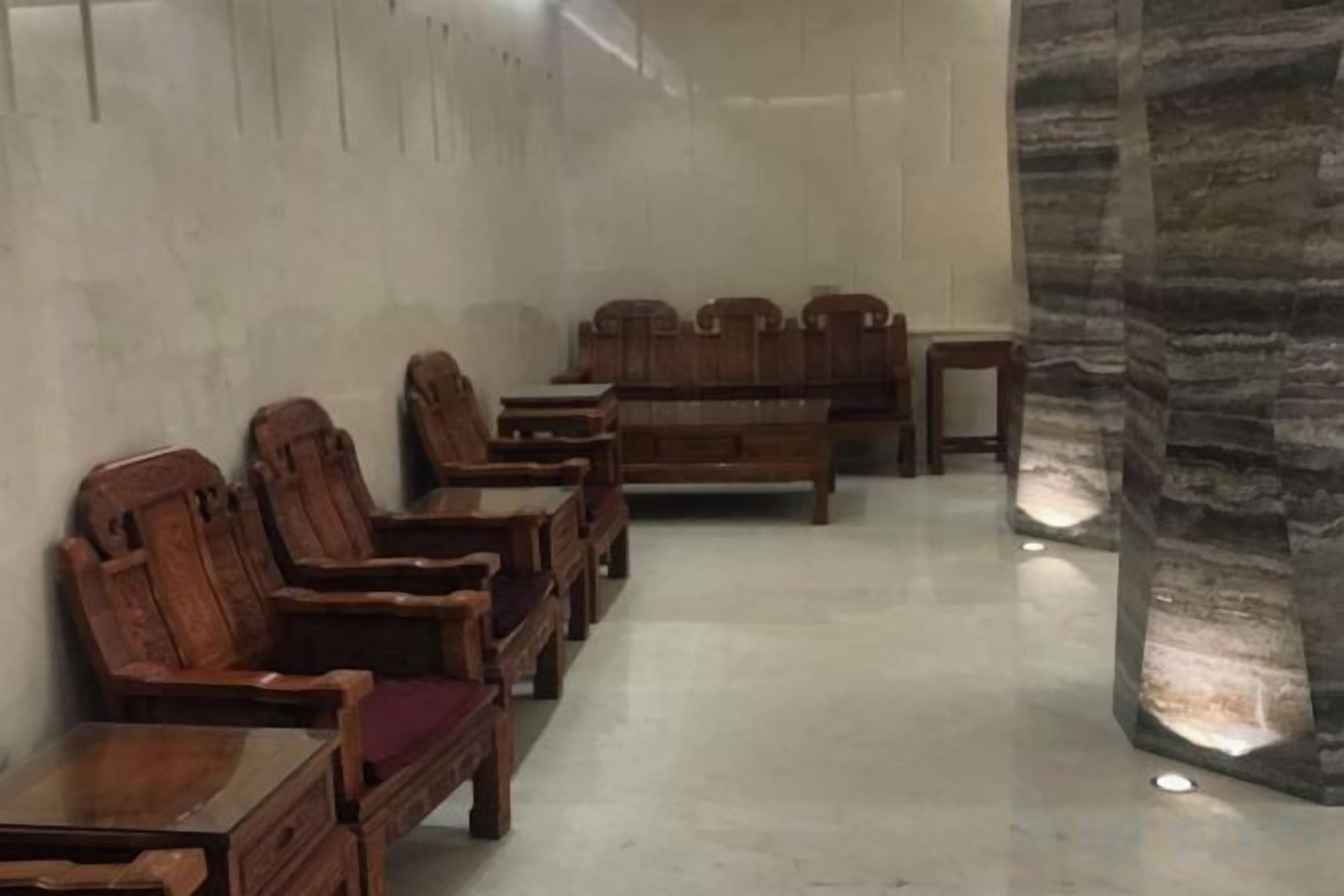 A room with wooden furniture arranged in rows, a stone pillar, and a plain wall.