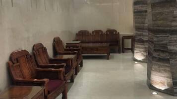A room with wooden furniture arranged in rows, a stone pillar, and a plain wall.