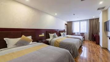 A hotel room with three beds, wooden flooring, a TV, and a window with curtains.