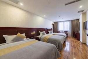 A hotel room with three beds, wooden flooring, a TV, and a window with curtains.