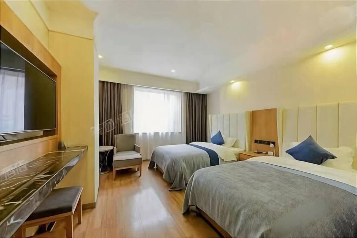 Habitación de hotel con dos camas, un escritorio, una silla, un televisor y una ventana con cortinas.