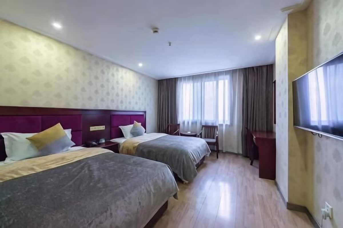 A hotel room with two beds, a desk, a chair, and a large window with curtains.