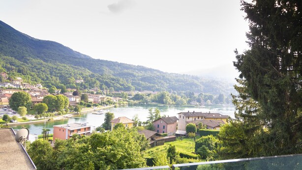 A riverside town with buildings, greenery, and a mountain backdrop.