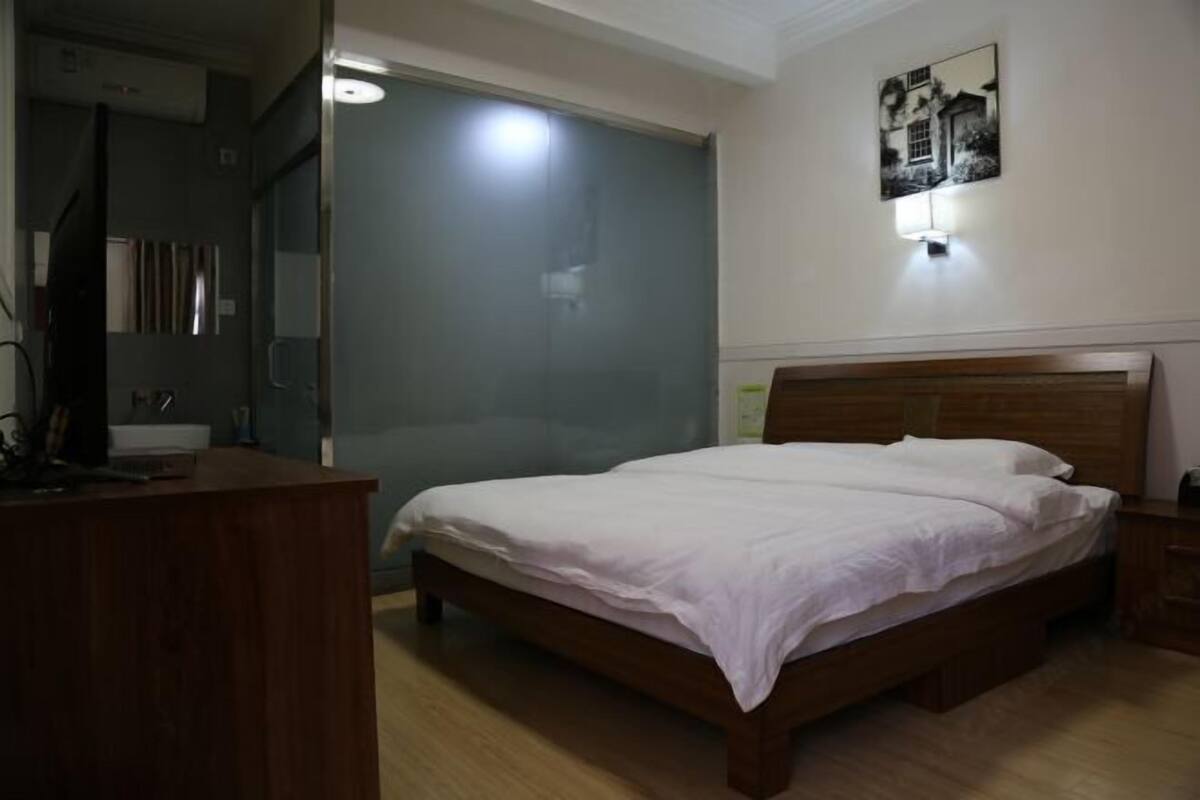 A bedroom with a wooden bed, a desk, and a glass door leading to a bathroom.