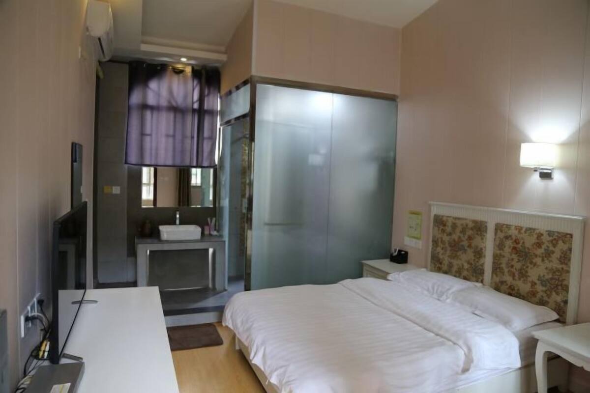 A hotel room with a bed, a desk, a mirror, a bathroom with a sink, and a shower.