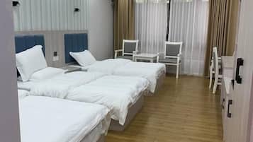 A hotel room with three beds, a small table, two chairs, and a window with sheer curtains.