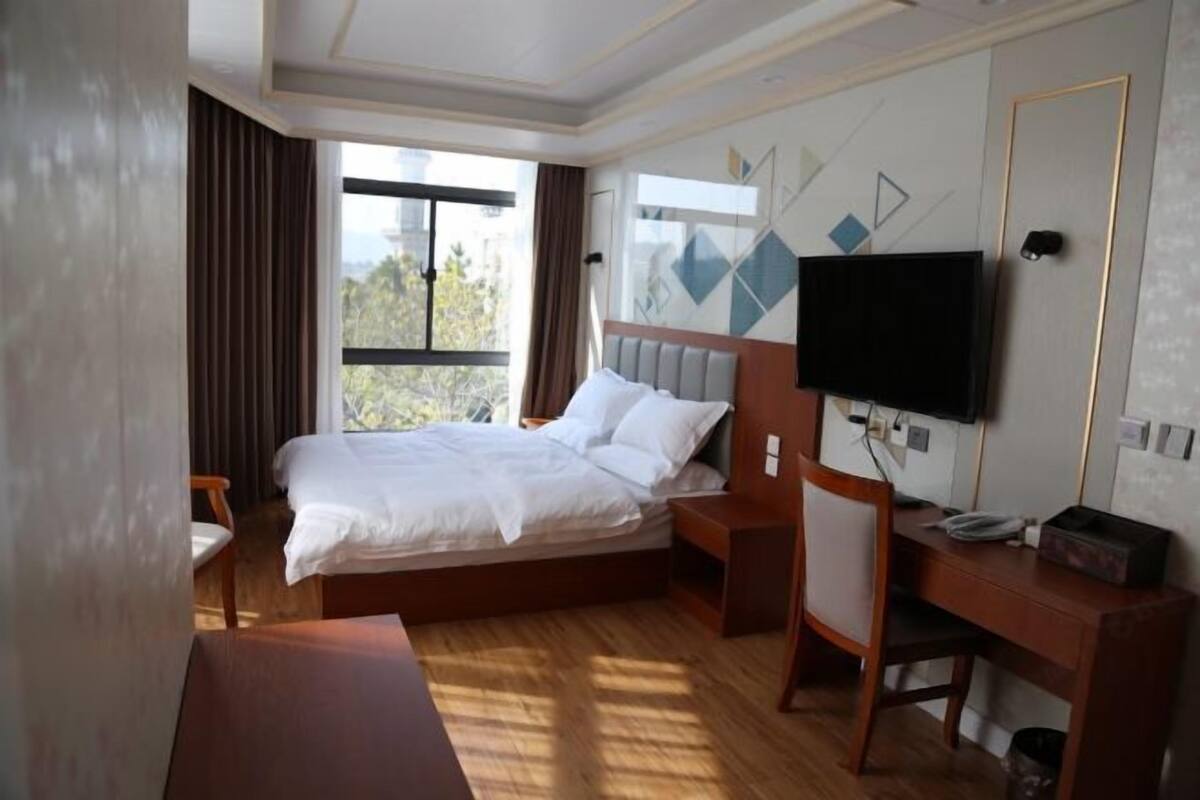 A hotel room with a bed, a desk, a chair, a TV, and a window with curtains.