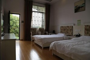 Quarto de hotel com duas camas, uma escrivaninha, uma cadeira, janela com cortinas e vista para o verde lá fora.