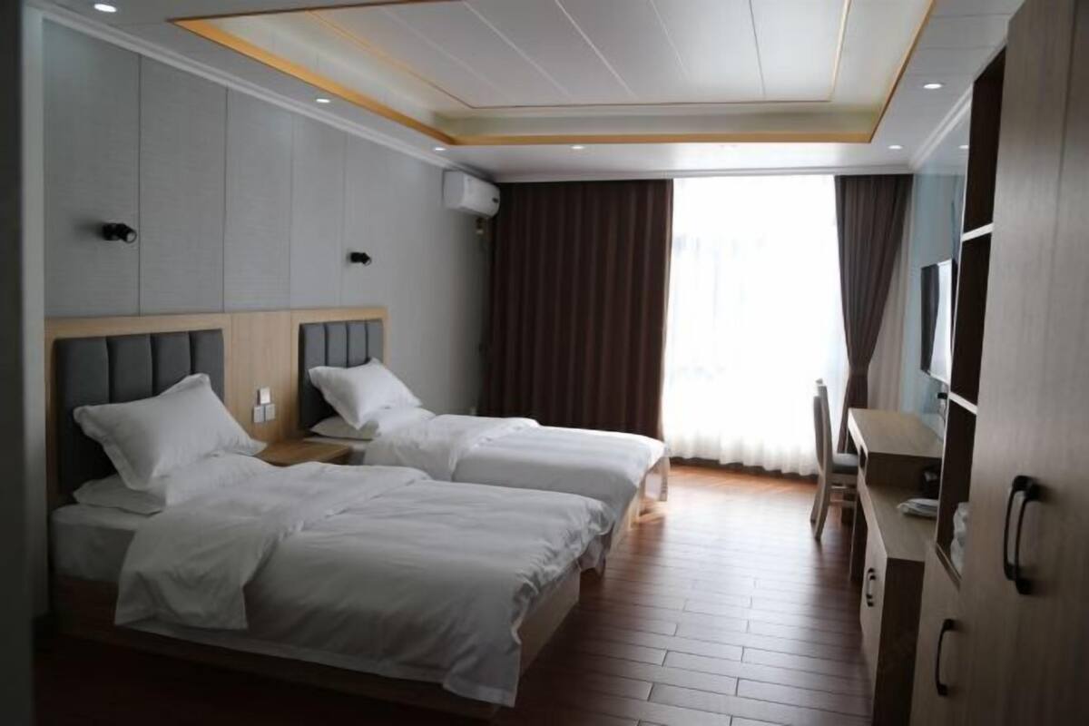 A hotel room with two beds, a desk, a TV, and a window with curtains.