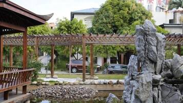 A traditional pavilion with a wooden roof, a rock garden, and a pond.
