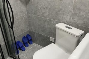 Un baño con inodoro, zona de ducha y un par de pantuflas azules en el suelo.
