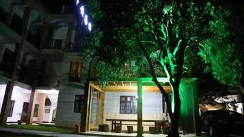 A building with a covered seating area and a tree with green lighting.
