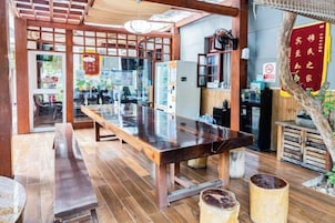 Interior de restaurante con una larga mesa de madera, zona de estar y una barra.