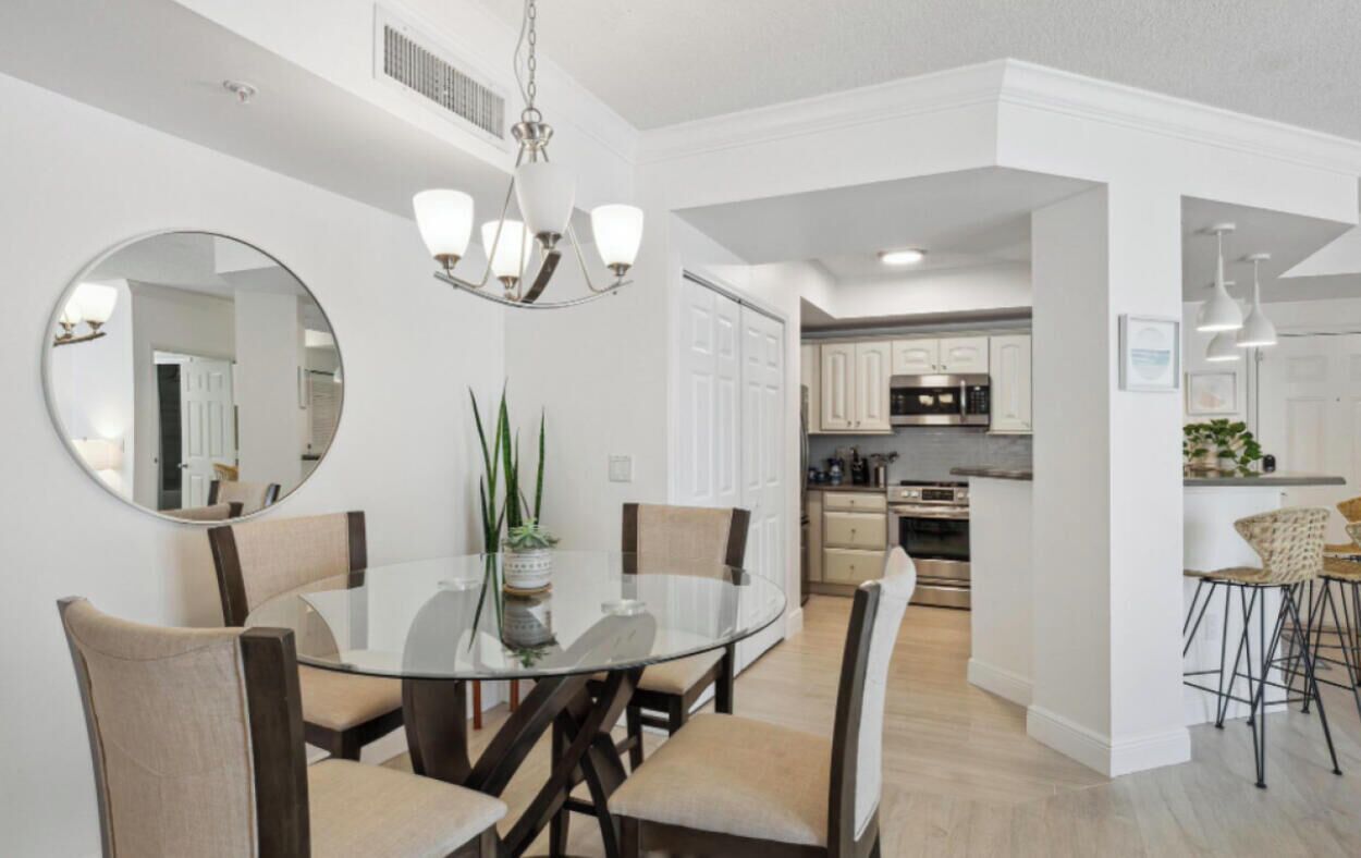 A modern kitchen with white cabinets, a central island, and a dining area with a glass table and chairs.