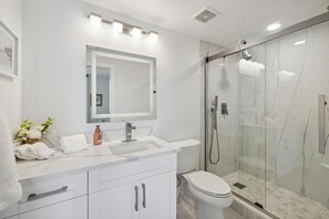 A modern bathroom with a white vanity, a large mirror, a glass-enclosed shower, and a toilet.