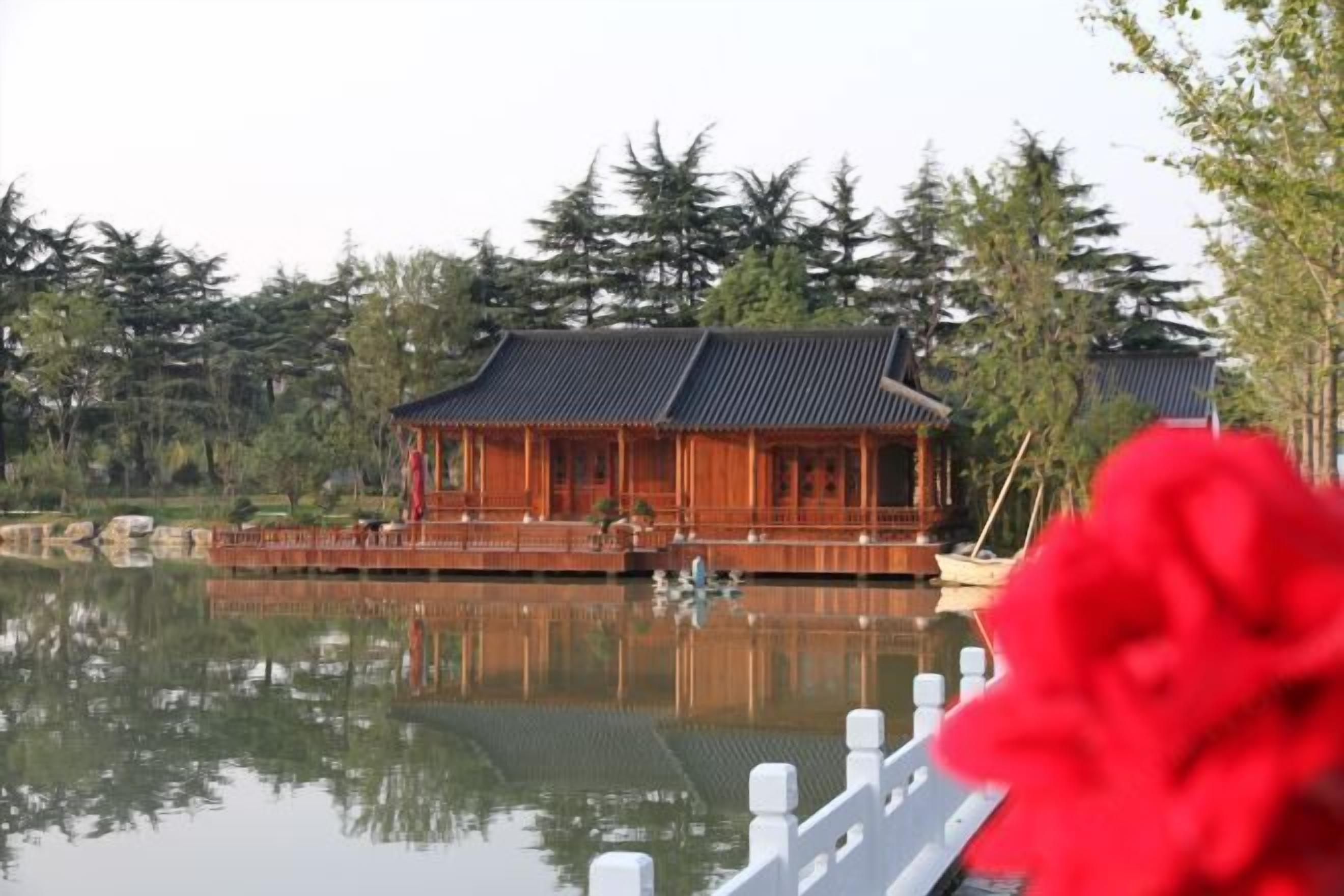 Un edificio de madera tradicional con techo de tejas, reflejado en aguas tranquilas, rodeado de árboles.