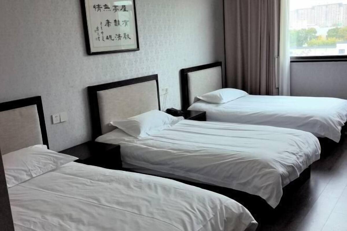 Quarto de hotel com três camas de solteiro, uma obra de arte emoldurada na parede e uma janela com cortinas.