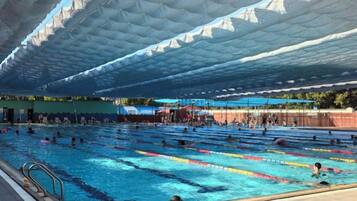 An indoor swimming pool with multiple lanes, a covered roof, and a spectator area.