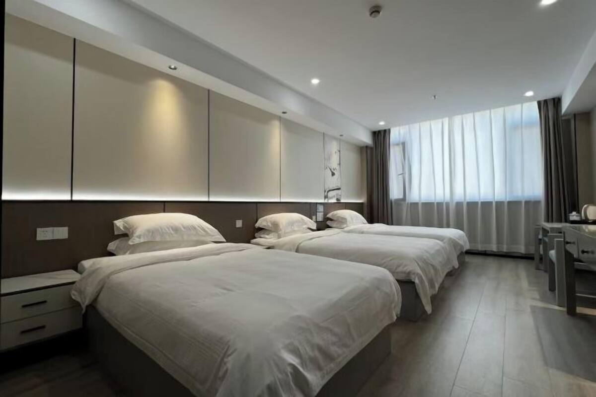 Quarto de hotel moderno com duas camas, uma escrivaninha e uma janela grande com cortinas.