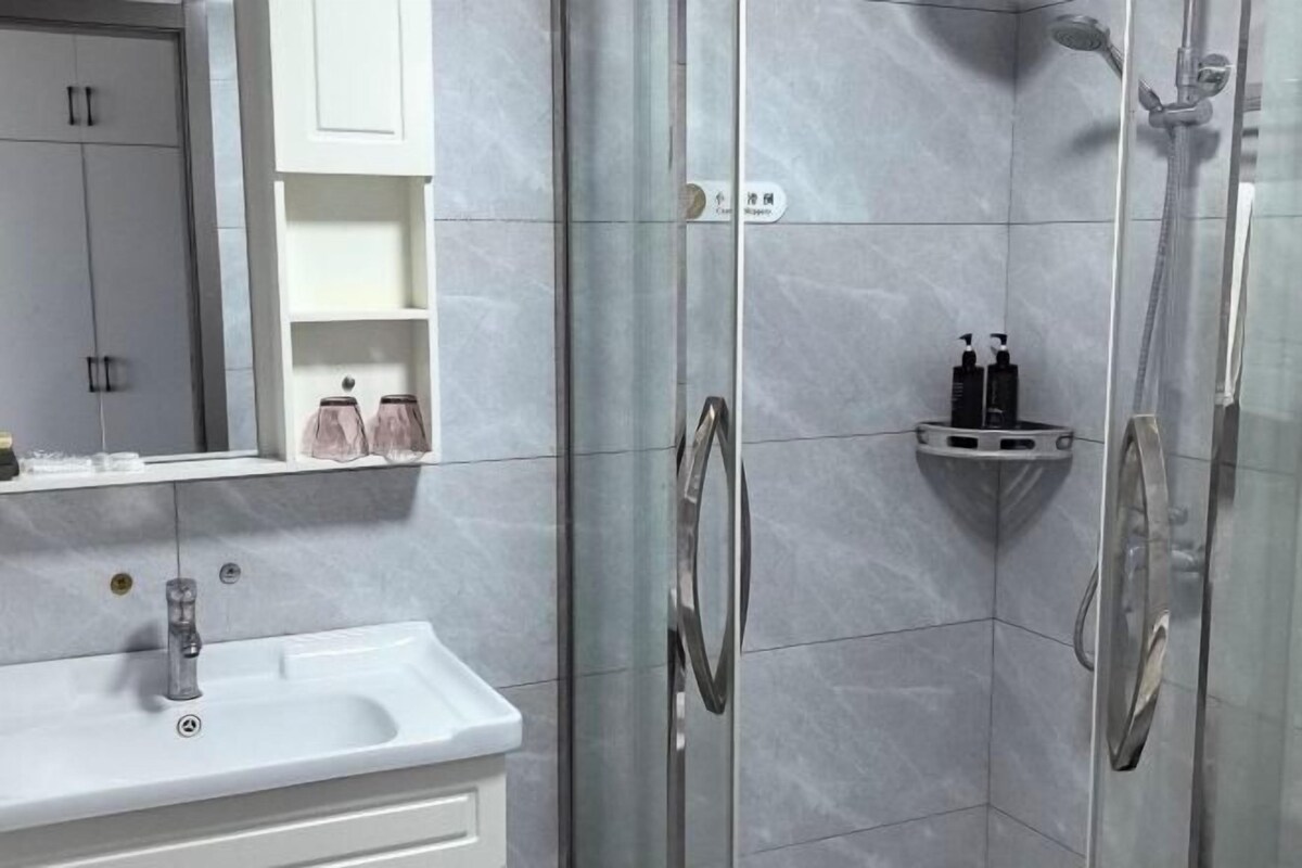 A modern bathroom with a white sink, glass shower enclosure, and storage cabinets.