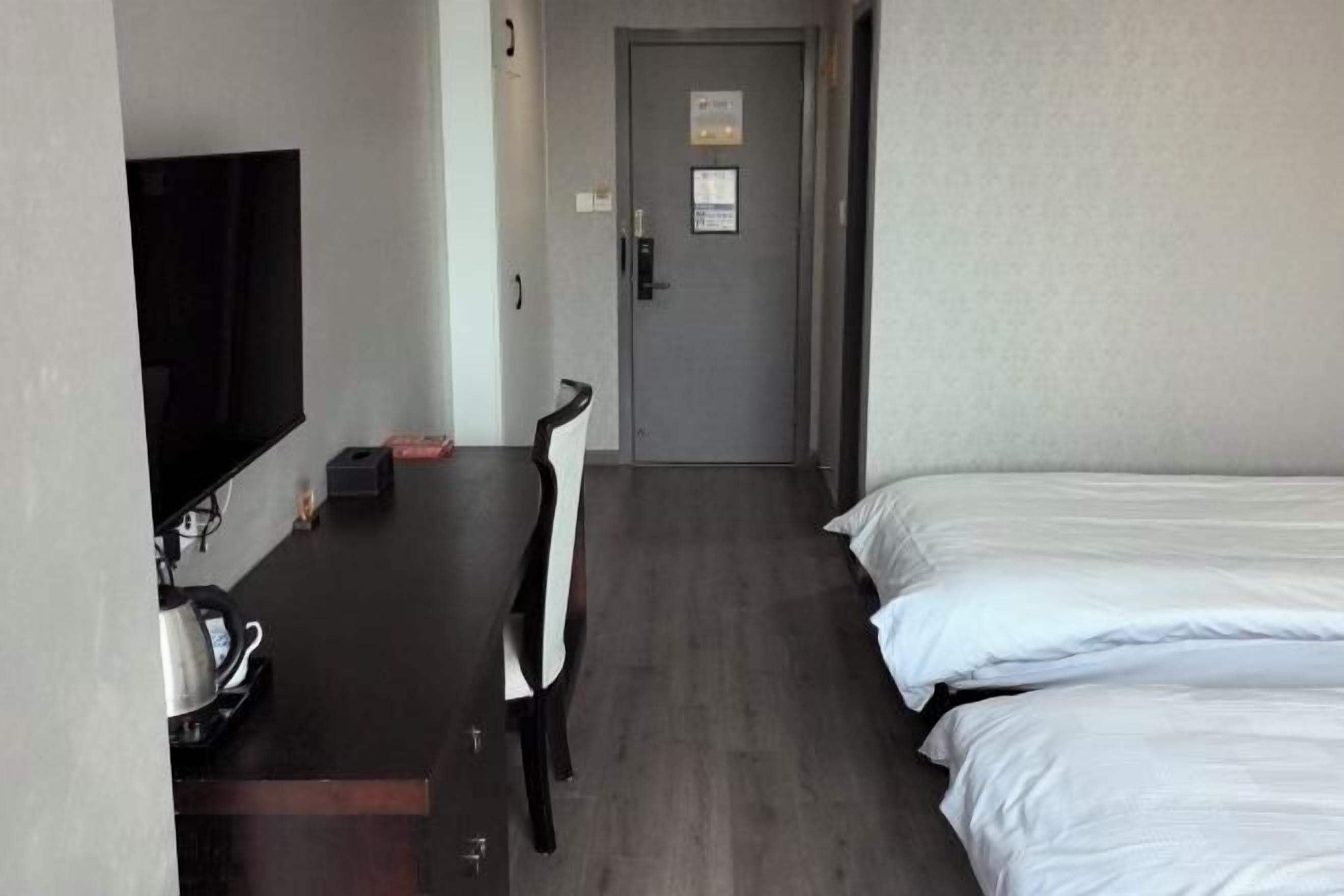 Hotellihuone, jossa on sänky, työpöytä tuolilla, televisio ja ovi, jossa on kyltti.