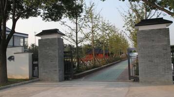 A gated entrance with a pathway leading to a building, surrounded by trees and a clear sky.