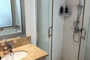 A bathroom with a marble sink, a glass shower enclosure, and a shelf with toiletries. - Baolong Furui Hotel (Changzhou)