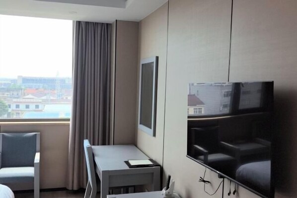 A hotel room with a large window, a flat-screen TV, a desk, and a chair. - Baolong Furui Hotel (Changzhou)