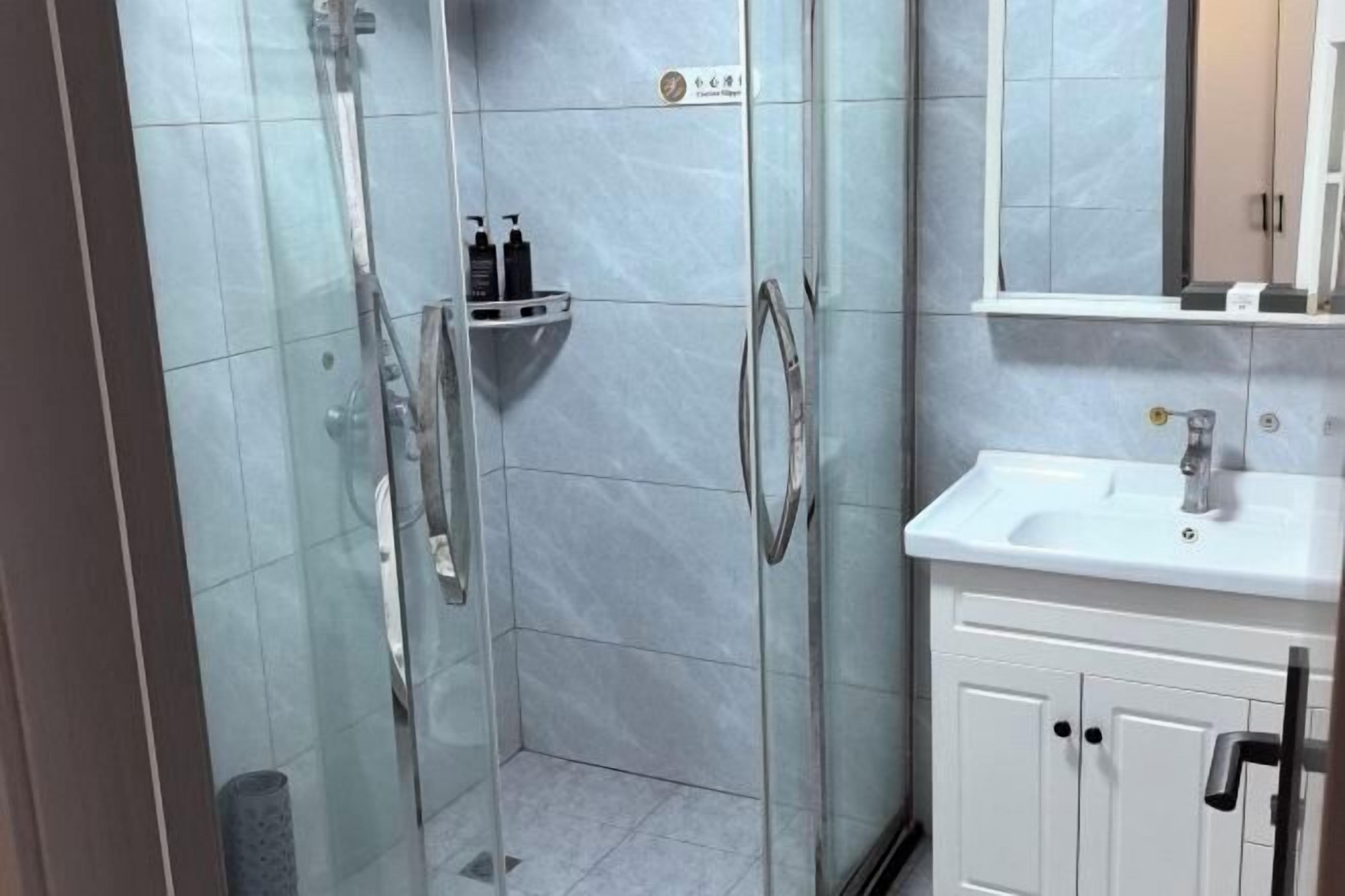 Un baño moderno con ducha envuelta en vidrio, un lavabo blanco y un espejo sobre él.
